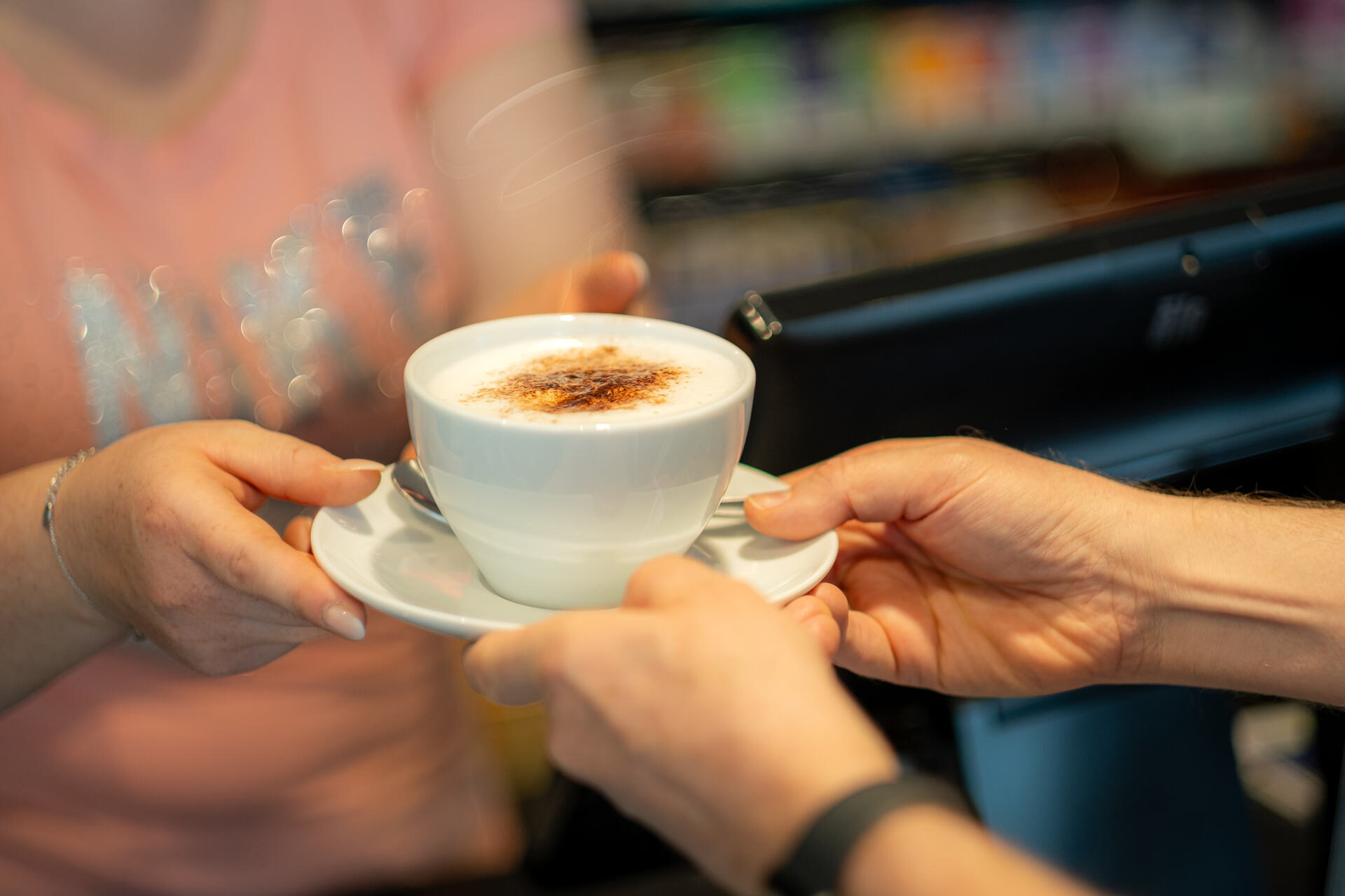 Verkäuferin reicht Kunden eine Tasse Cappuccino